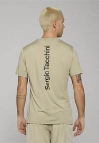 Béžové tričko s krátkými rukávy a vertikálním černým logem na zadní straně. Hladký materiál s volným střihem. Minimalistický design bez vzorů.