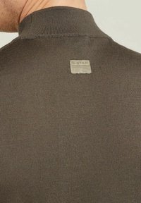 Tessuto marrone a coste con design a collo alto. Presenta un'etichetta rettangolare con il marchio "G-STAR" cucita sul retro.