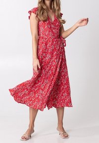Rotes Blumenkleid mit kurzem Rüschensaum, knielang, aus leichtem Stoff. Es zeigt weiße und rosa Blumenmuster.