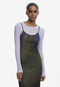 Gestreiftes Langarmoberteil in Helllila, unter einem ärmellosen, figurbetonten Kleid mit einem Farbverlauf in Dunkelgrün und Blau.