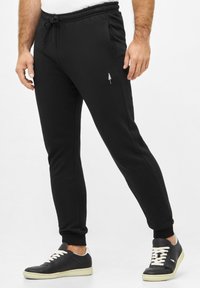 Schwarze Sweatpants mit elastischem Bund, seitlichen Taschen und ankles mit Bündchen. Verfügt über ein kleines gesticktes Baumdesign am Oberschenkel.