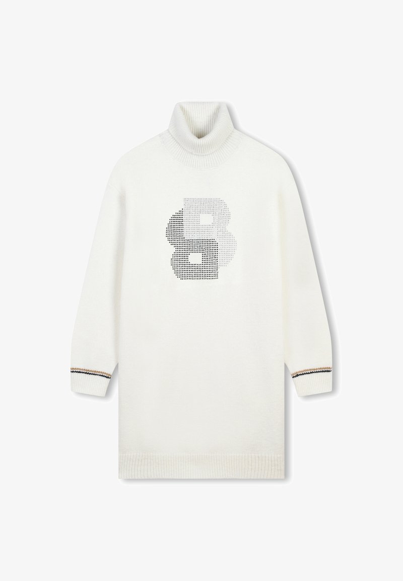 Pull en col roulé blanc à manches longues, avec un motif de pois noirs en forme de lettres "B" sur le devant et des accents rayés au niveau des poignets.