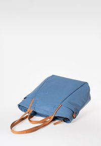 Borsa a tote in tessuto blu con manici in pelle beige. Presenta un design pulito e moderno con cuciture evidenti e un logo sottile impresso di lato.