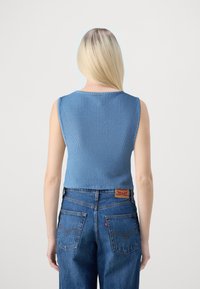 Blå strikket kort topp med rund hals, parret med høyhvide blå denimjeans med baklommer og en merkelapp.
