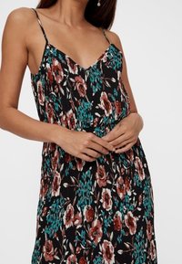 Mustakukkainen mekko säädettävillä ohutolkaimilla, jossa on punaisia ja turkooseja kukkia, teksturoitu kangas ja joustava vyötärö.