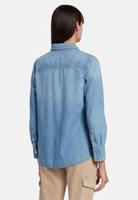 Camicia in denim azzurro chiaro con maniche lunghe, polsini con bottone e colletto classico. Presenta una trama liscia e un design con vestibilità rilassata.