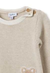 Suéter de punto beige con un cuello de canalé blanco, detalles en botones de madera y una aplicación de cara de oso en la parte delantera.