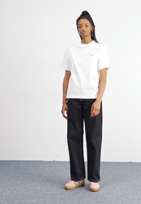 Witte katoenen T-shirt met een losse pasvorm, gecombineerd met high-waisted zwarte denim jeans en roze platform sneakers met groene accenten.
