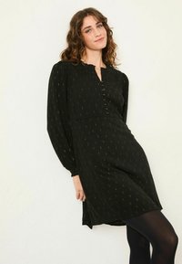 Schwarzes Kleid mit langen Ärmeln, durchgehender Knopfleiste und Rüschenausschnitt. Verfügt über ein goldfarbenes Muster auf dem Stoff, knielangen Schnitt und weichen Griff.