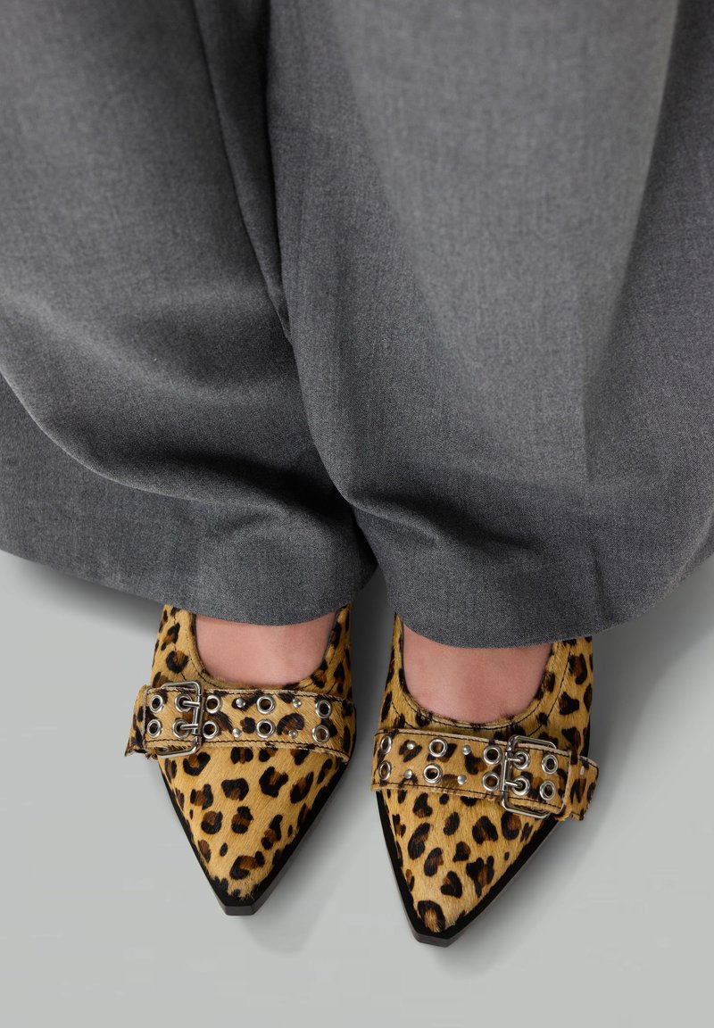 Luipaardprint schoenen met puntige neuzen en een suède textuur, voorzien van een gespsluiting en metalen accenten, gecombineerd met grijze wijde broek.