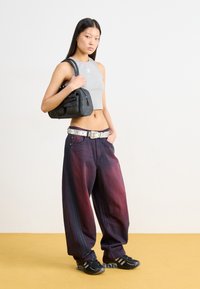 Gray crop top, baggy purple-red jeans with side stripes, silver belt with studs, black handbag, and black athletic shoes.