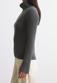 Suéter de cuello alto gris con rayas, de manga larga, con un diseño ajustado y textura suave, combinado con un pantalón de color claro.