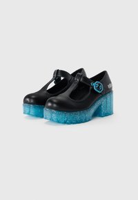 Chaussures à plateforme noires avec un design à sangle T, présentant un talon translucide bleu texturé avec des paillettes et un détail de boucle sur le côté.
