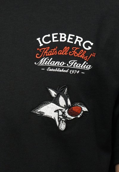 Μαύρο ύφασμα με κεντημένο κείμενο «ICEBERG 'That's all Folks!' Μιλάνο Ιταλία Ιδρύθηκε το 1974» και καρτούν πρόσωπο λύκου με κόκκινη μύτη.