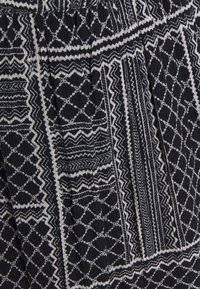 Telar de tela negra texturizada con patrones geométricos blancos, que presenta diseños en zigzag y rombo. Detalle con pliegues visible en toda la prenda.