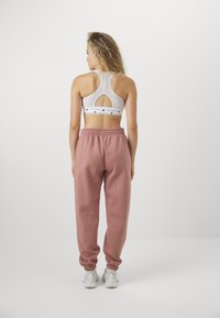 Λευκό αθλητικό σουτιέν με κοψίματα στην πλάτη και μαύρη λογότυπη ζώνη, σε συνδυασμό με ροζ ψηλόμεσες φόρμες με ελαστική μέση και λευκά αθλητικά παπούτσια.