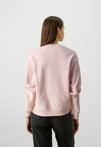 Felpa rosa chiaro con vestibilità rilassata, colletto a girocollo a coste e maniche lunghe, abbinata a jeans neri. Tessuto morbido e design minimale.