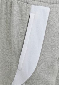 Graue Jogginghosen mit weichem Material, seitlichen Taschen und einem kontrastierenden weißen Panel. Der Bund ist elastisch für zusätzlichen Komfort.
