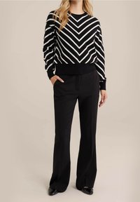 Czarny i biały sweter dzianinowy w zygzakowy wzór z okrągłym dekoltem, prążkowanymi mankietami i wykończeniem, w zestawieniu z czarnymi spodniami o wysokim stanie.