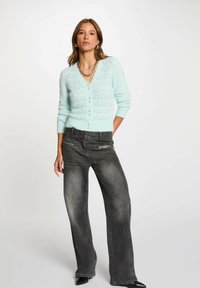 Cardigan blu pallido, lavorato a maglia, con scollatura a V, intricato motivo a zigzag e piccoli bottoni, abbinato a jeans grigi scuri a gamba larga.