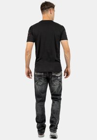 T-shirt nero a maniche corte con colletto a girocollo, abbinato a jeans grigi sbiaditi con cuciture decorative e due tasche posteriori.