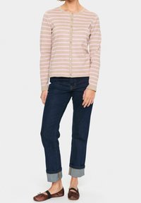 Ljusbeige och rosa randig cardigan med knappstängning, i kombination med mörka denimjeans. Jeansen har uppvikta fållar, och platta skor fulländar outfiten.