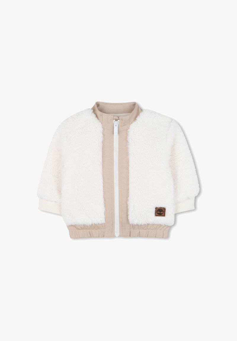 Crème kunstbontjack met beige stofpanelen. Heeft een witte rits, ribbelmanchetten en een elastische tailleband. Timberland logo patch aan de voorkant.