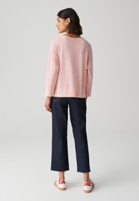 Hellrosa, locker sitzender Strickpullover, kombiniert mit dunkelblauen, weit geschnittenen Jeans mit rohen Säumen und weißen Turnschuhen mit roten Akzenten.