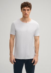 Lichtgrijs t-shirt met korte mouwen, ronde hals, zacht katoenmateriaal, iets ontspannen pasvorm, vlakke naden, gedragen met donkere broek.