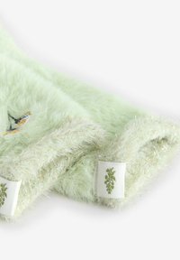 Tela de piel sintética verde claro con una textura suave, realzada por hilos metálicos a lo largo de los bordes. Presenta un pequeño diseño de mariposa bordada.