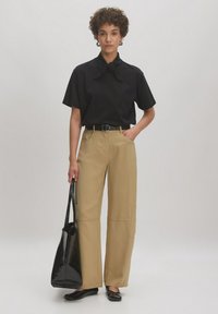 Zwart short-sleeve top met een strik kraag, beige wijde broek, zwarte riem, zwarte tas en platte schoenen. De broek heeft zijzakken.