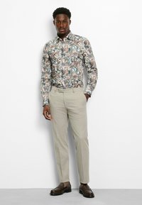 Button-up shirt with a multicolored floral and leaf pattern, paired with light-colored trousers and dark brown loafers.