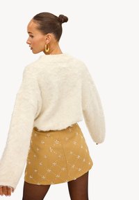 Suéter crema esponjoso con mangas extragrandes combinado con una minifalda mostaza estampada que presenta detalles florales y un acabado texturizado.