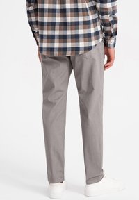 Pantalons en coton gris à coupe droite, présentant une texture lisse et des poches arrière, associés à une chemise à carreaux marron et bleu.