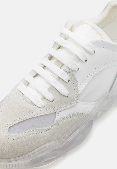 White sneaker featuring a combination of smooth leather, soft suede, and transparent rubber outsole. Laces are white, with grey accents for texture.