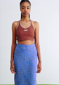 Brun cropped halterneck topp med lys trim og logo, parret med et blåt mønstret midi-skjørt med blomsterlignende designs i hvidt og sort.