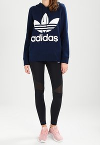 Mörkblå hoodie med vit Adidas-logotyp, svarta leggings med meshdetaljer och rosa träningsskor. Enkelt, avslappnat sportklädsel.