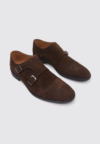 Zapatos de ante marrón con doble correa y hebillas plateadas; puntera afilada y forro de cuero liso; suela plana negra; diseño elegante con acentos mínimos.