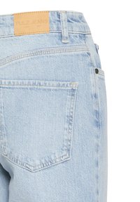 Svijetloplave traperice izbliza koje prikazuju stražnji džep i oznaku od smeđe kože s natpisom "PULZ JEANS".