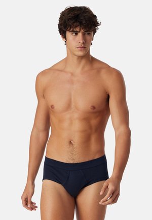 Slip blu navy in tessuto liscio, con design aderente, fascia larga in vita e pannello frontale di supporto. Linee pulite e dettagli minimi.