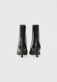 Zwarte leren enkellaarzen met een puntige neus, slanke stilettohak en gouden ritsdetail aan de zijkant. Glad, glanzende afwerking.
