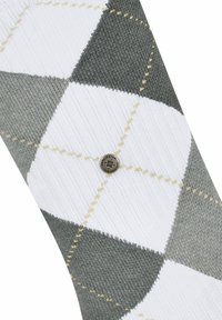 Grau-weiße Socken im Argyle-Muster mit strukturiertem Strick. Mit einem silbernen Logo-Button im Knöchelbereich, akzentuiert durch gelbe Nähte.