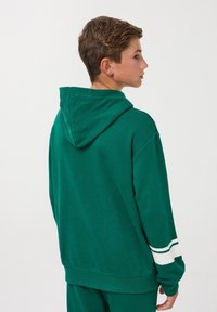 Felpa verde in cotone con tasca a marsupio frontale e accenti a righe bianche sulle maniche. Presenta un grande cappuccio e una vestibilità comoda.