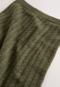 Olive green textured fabric displaying a cable-knit pattern, with a ribbed waistband and soft, fuzzy appearance.