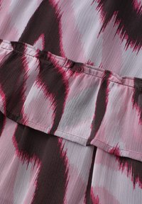 Tissu avec un motif abstrait rose, noir et blanc présentant une couture horizontale et un détail froncé.