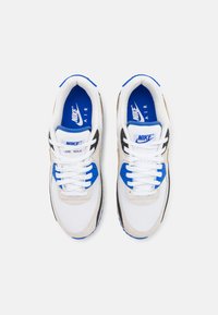 Sapatilhas brancas e cinzas com detalhes azuis. Apresentam materiais de malha e camurça, design de atacadores e marca Nike visível na língua.