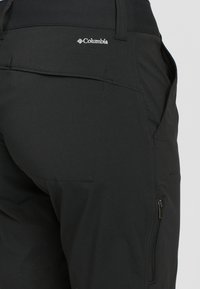 Pantaloni neri da esterno realizzati in tessuto liscio. Presentano una tasca posteriore e una tasca laterale con zip. Logo Columbia ricamato in vita.