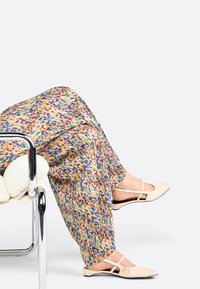 Pantaloni a gamba larga colorati e con fantasia, nei toni del blu, marrone e crema; abbinati a eleganti ciabatte beige chiaro con punta affusolata.