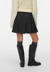 Szara spódnica w kształcie dzwonu wykonana z fakturowanej tkaniny, zestawiona z czarnymi skórzanymi kozakami do kolan i szarymi skarpetkami crew. Widok z tyłu ukazuje brzeg spódnicy i detale butów.