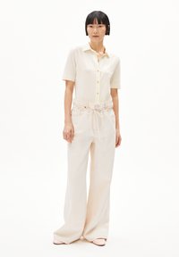 Camicetta corta a maniche corte di colore crema abbinata a pantaloni a gamba larga beige chiaro e scarpe rosa pallido; design semplice e texture dei tessuti morbide.